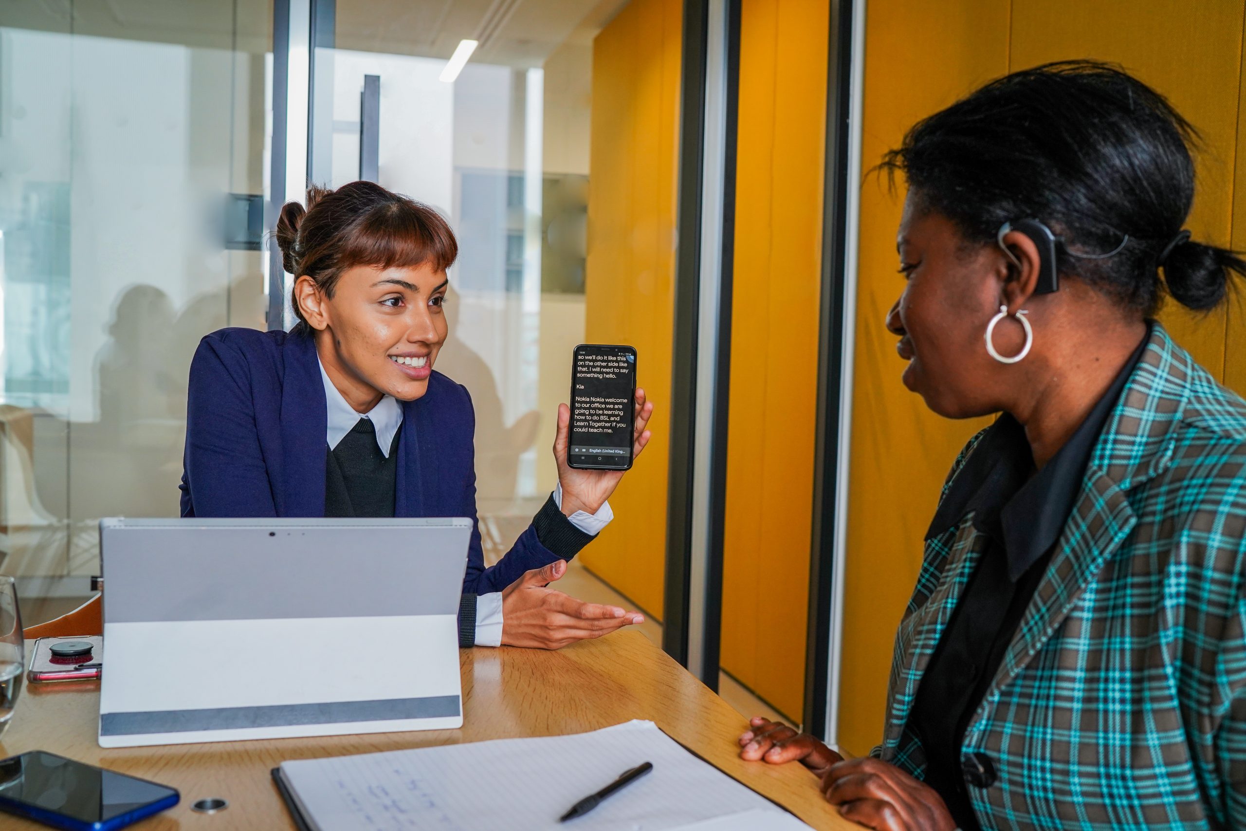 Deaf person being shown a text on a smartphone by a colleague in meeting room.