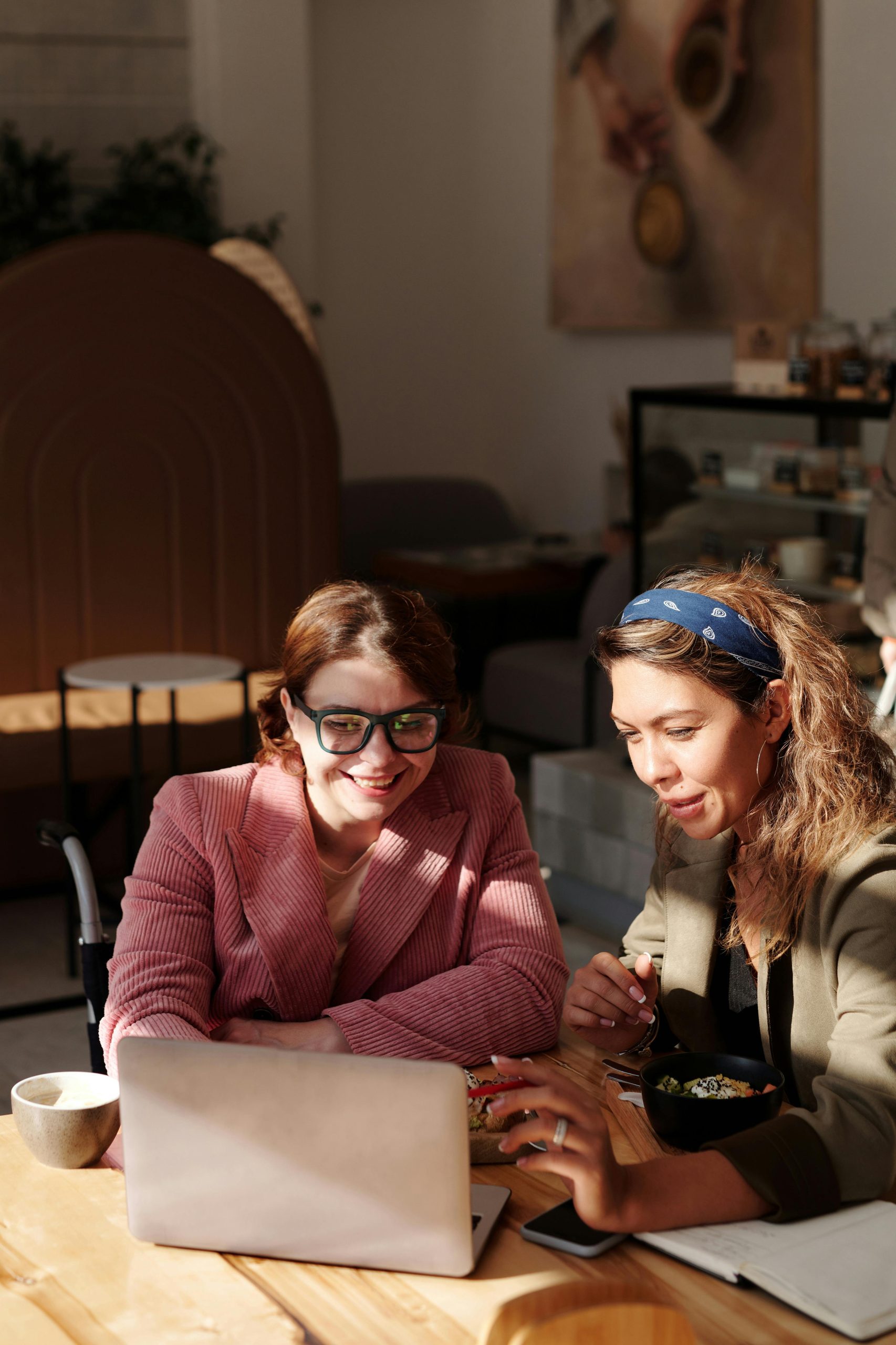 Two women sat at a table discussion the contents displayed on a laptop. The Lady to the left in the pink Jacket is sat in a wheelchair.