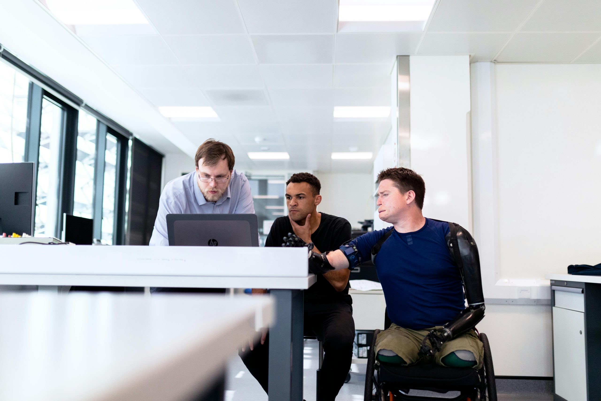 People sat at a bench discussing a project the person to the right is in a wheelchair and has prosthetic limbs