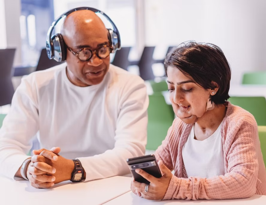 inclusion: a man with headphone watching a phones screen which is held by a women with disabilities